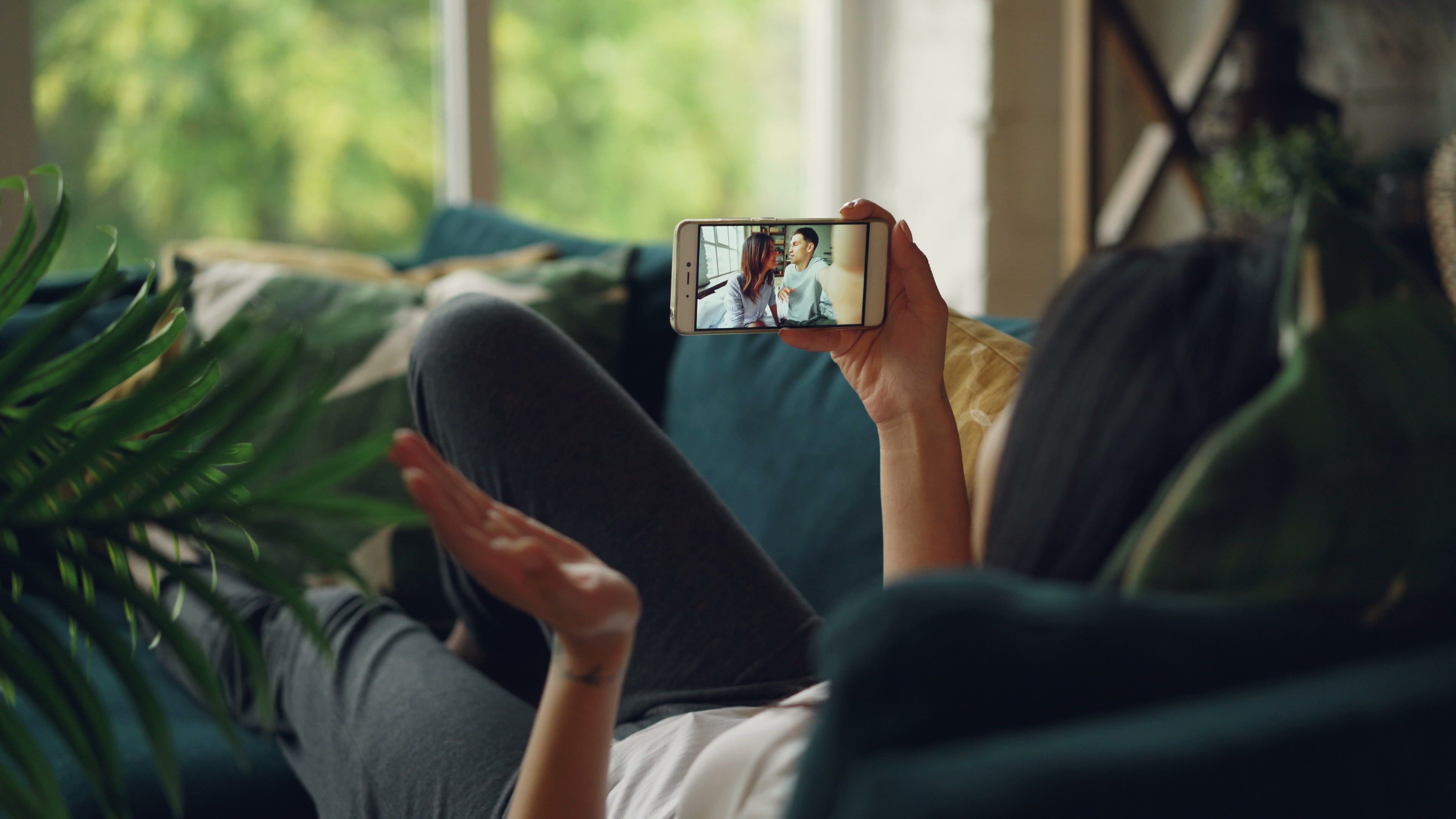 Person liegt auf dem Sofa und schaut ein Video auf dem Smartphone